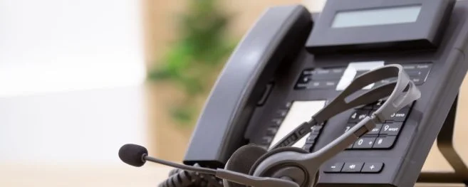 A close-up of a telephone and headset on a desk